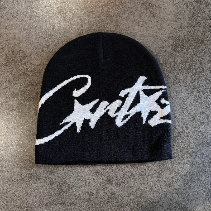 Black knit beanie with white script lettering on a textured surface