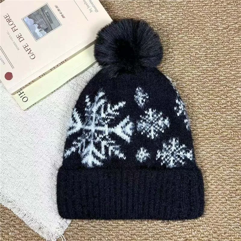 Black pom pom beanie with white snowflake motifs and a folded cuff