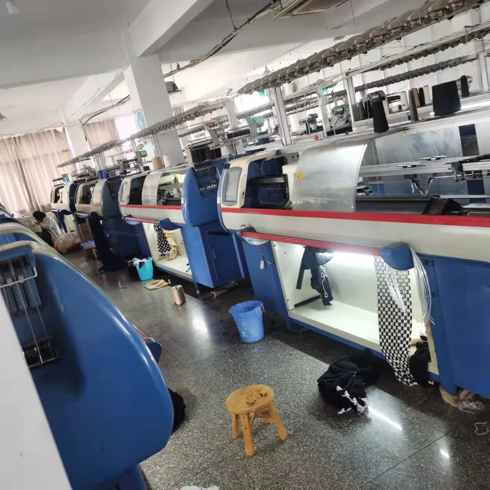 Blue and white flat bed knitting machines with hanging knitted panels