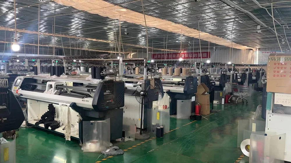 Flat bed knitting machines and yarn cones on a green workshop floor