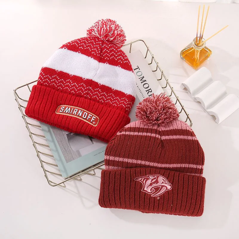 Red and burgundy striped pom pom beanies with sewn front patches