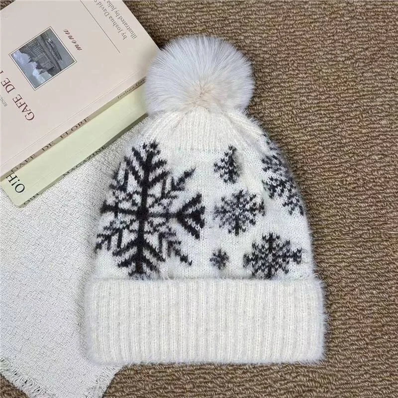 White pom pom beanie with black snowflake motifs and a folded cuff